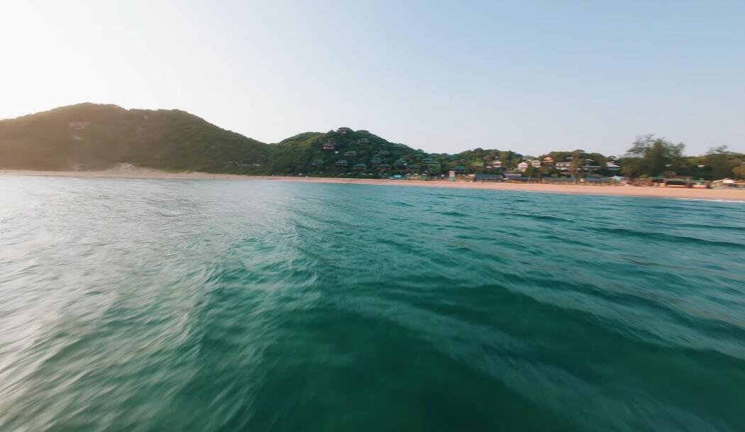 Low FPV pass over turquoise water towards a beach resort